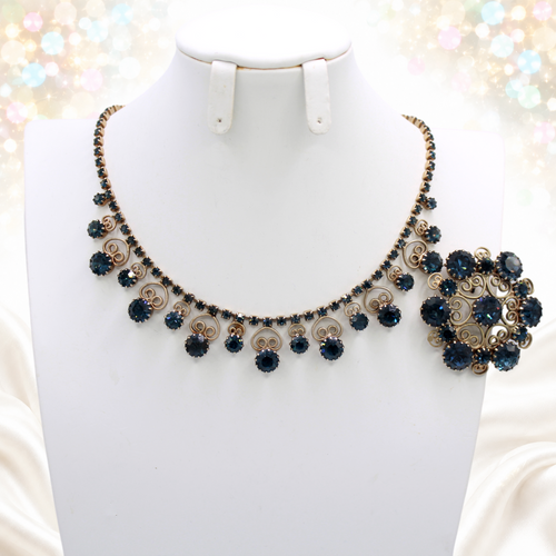 Close-up of graduated dark blue rhinestone necklace with heart scrollwork and circular brooch
