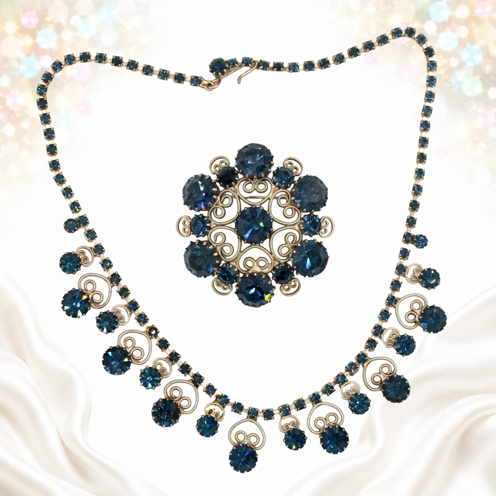 Dark blue rhinestone Juliana necklace and round scrollwork brooch displayed separately