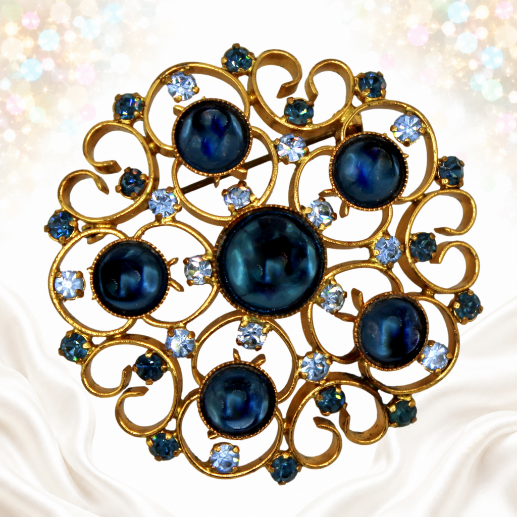 Vintage Juliana blue Lucite cabochon and light blue rhinestone heart-scroll brooch in gold-tone metal, front view